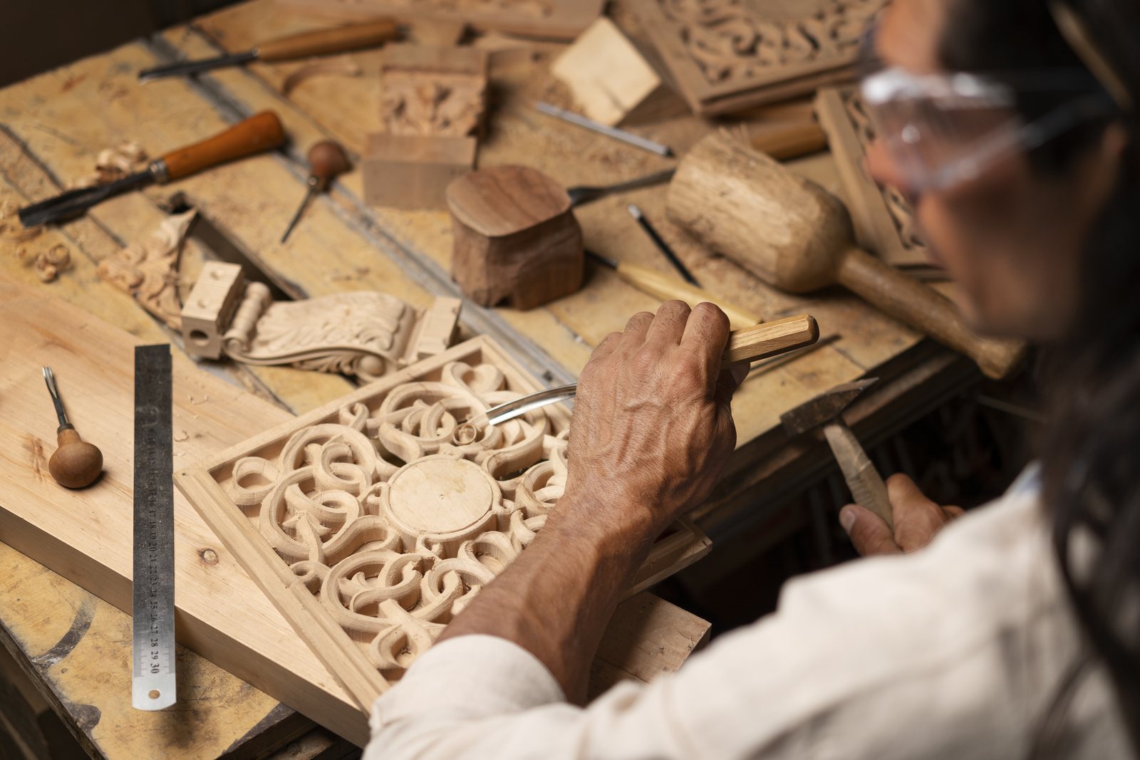 Artisan hand-carving an ornate scrollwork panel at a workbench full of chisels