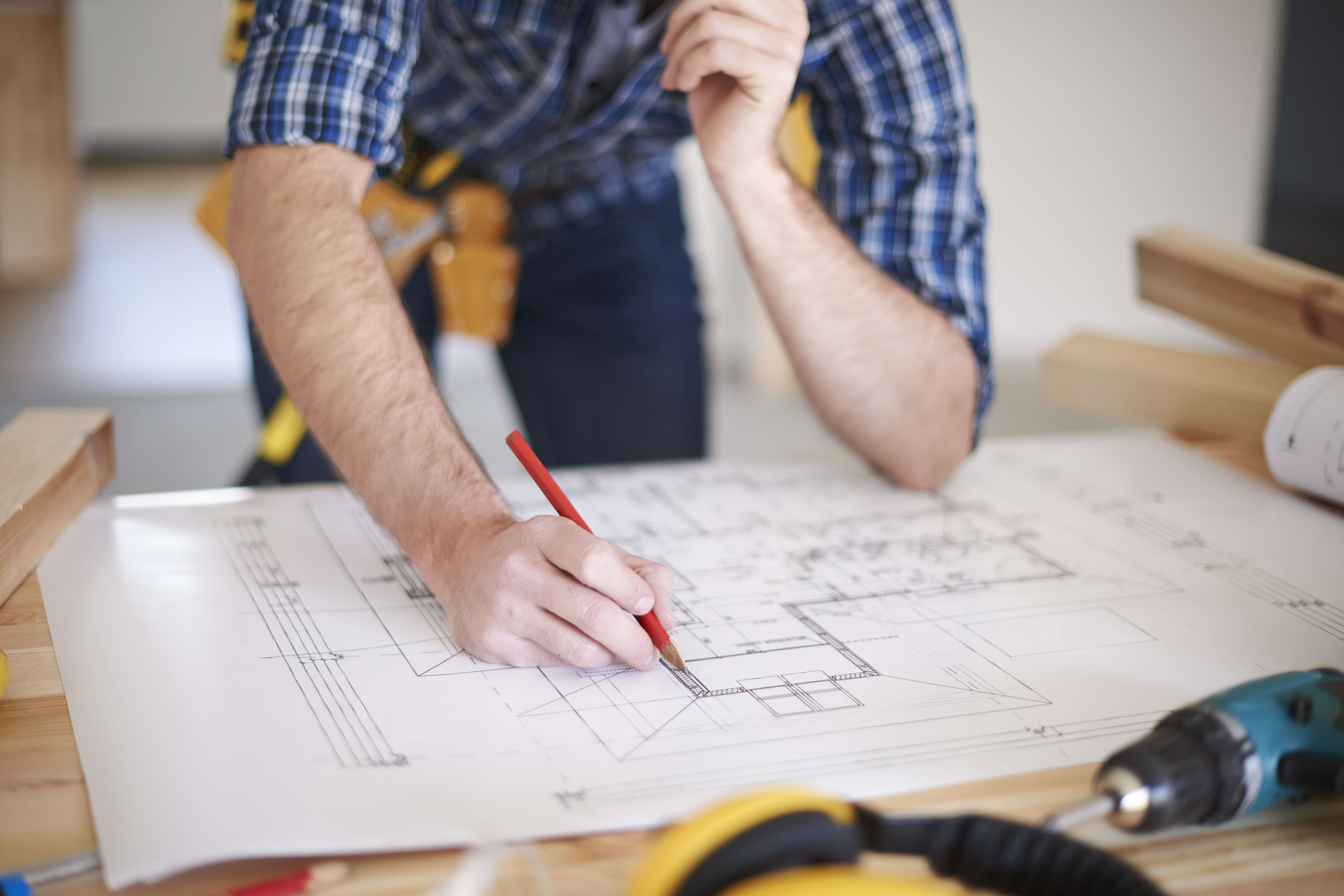 A detailer working over a millwork drawing with a scale rule and pencil
