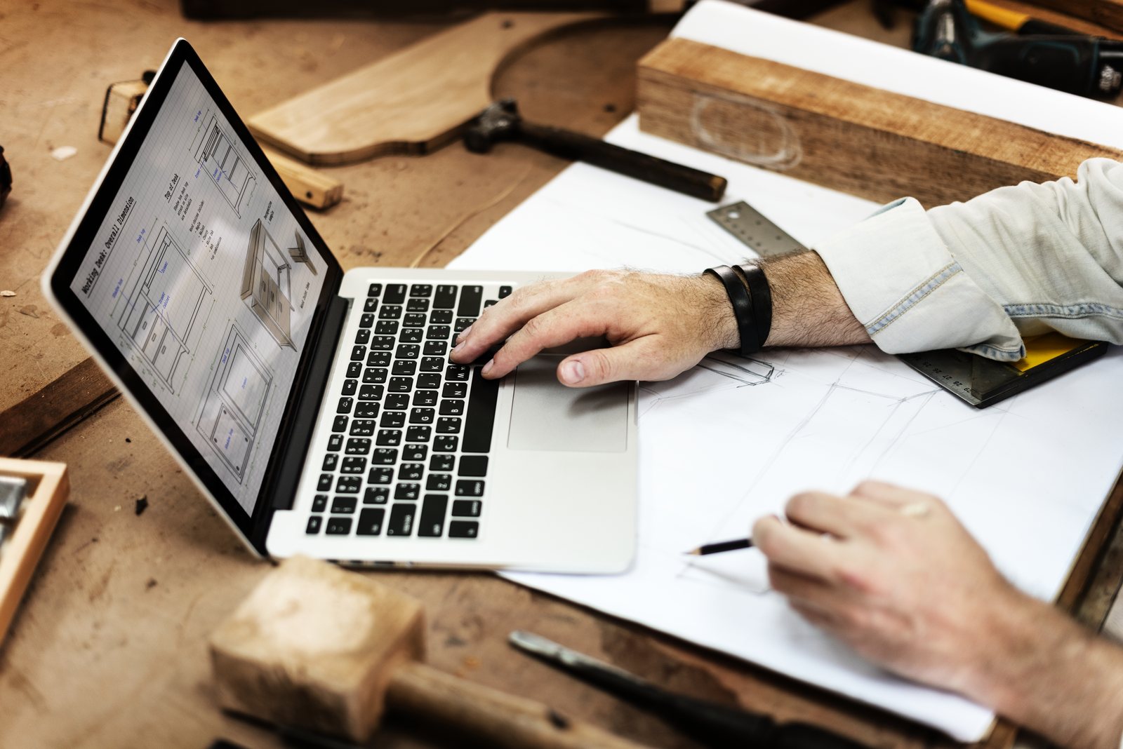 Laptop showing a software plan next to a hand-drawn sketch on a workbench