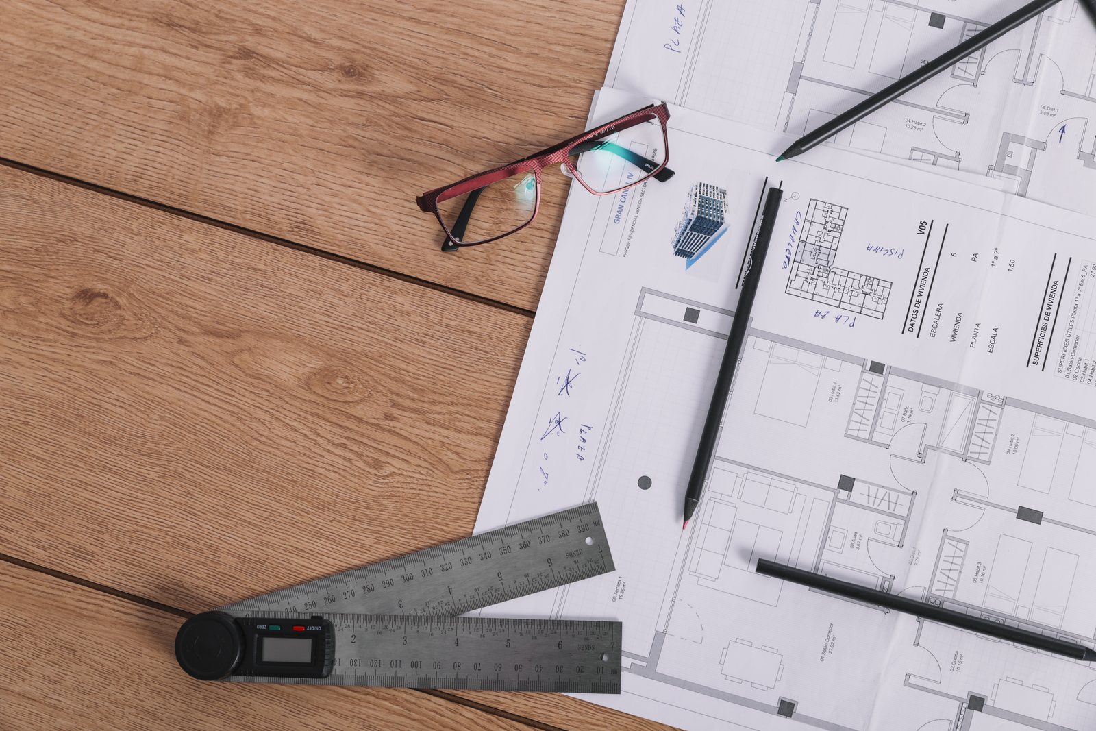 Blueprint with a ruler, glasses and pencils laid across it on a wood desk