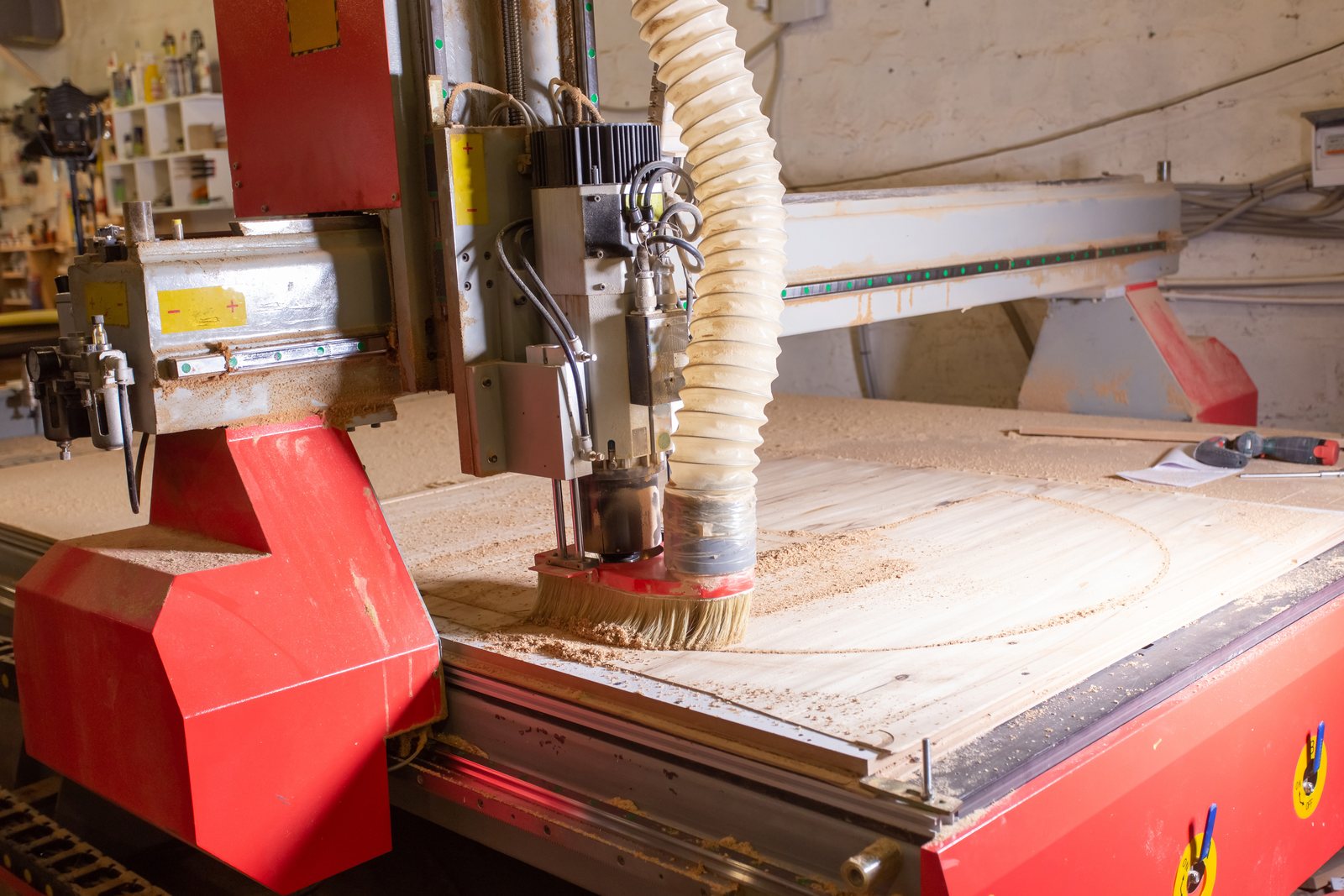 CNC router head with a dust-collection hose and brush positioned over a partly-cut wood panel