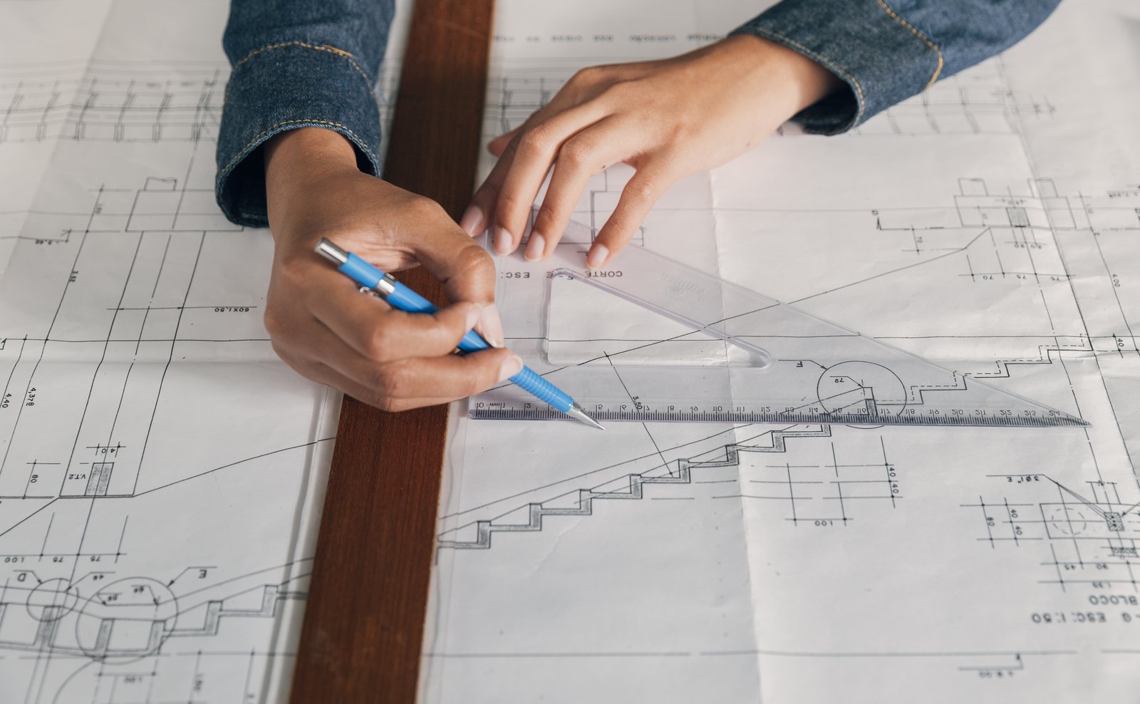 Hands using a set square and pencil to mark up a staircase detail on a blueprint