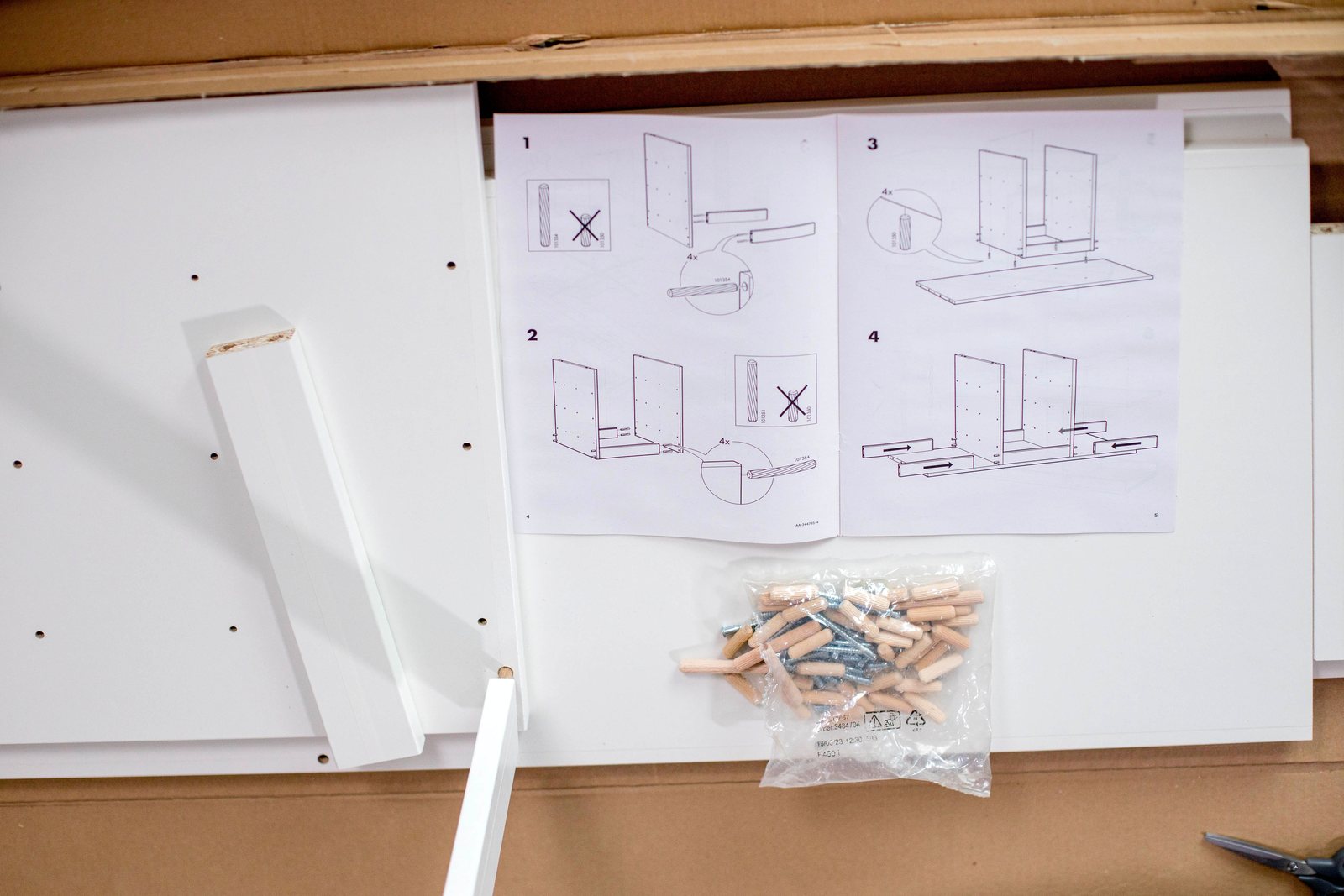 Flat-pack cabinet assembly instructions laid out beside panels, dowels and screws
