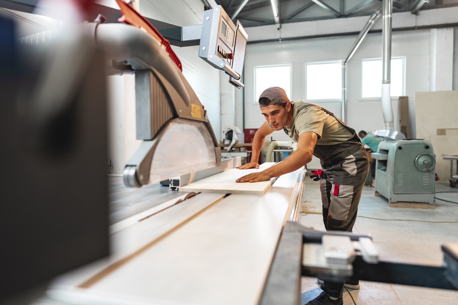 Worker guiding a panel through a beam saw on the shop floor of a furniture factory