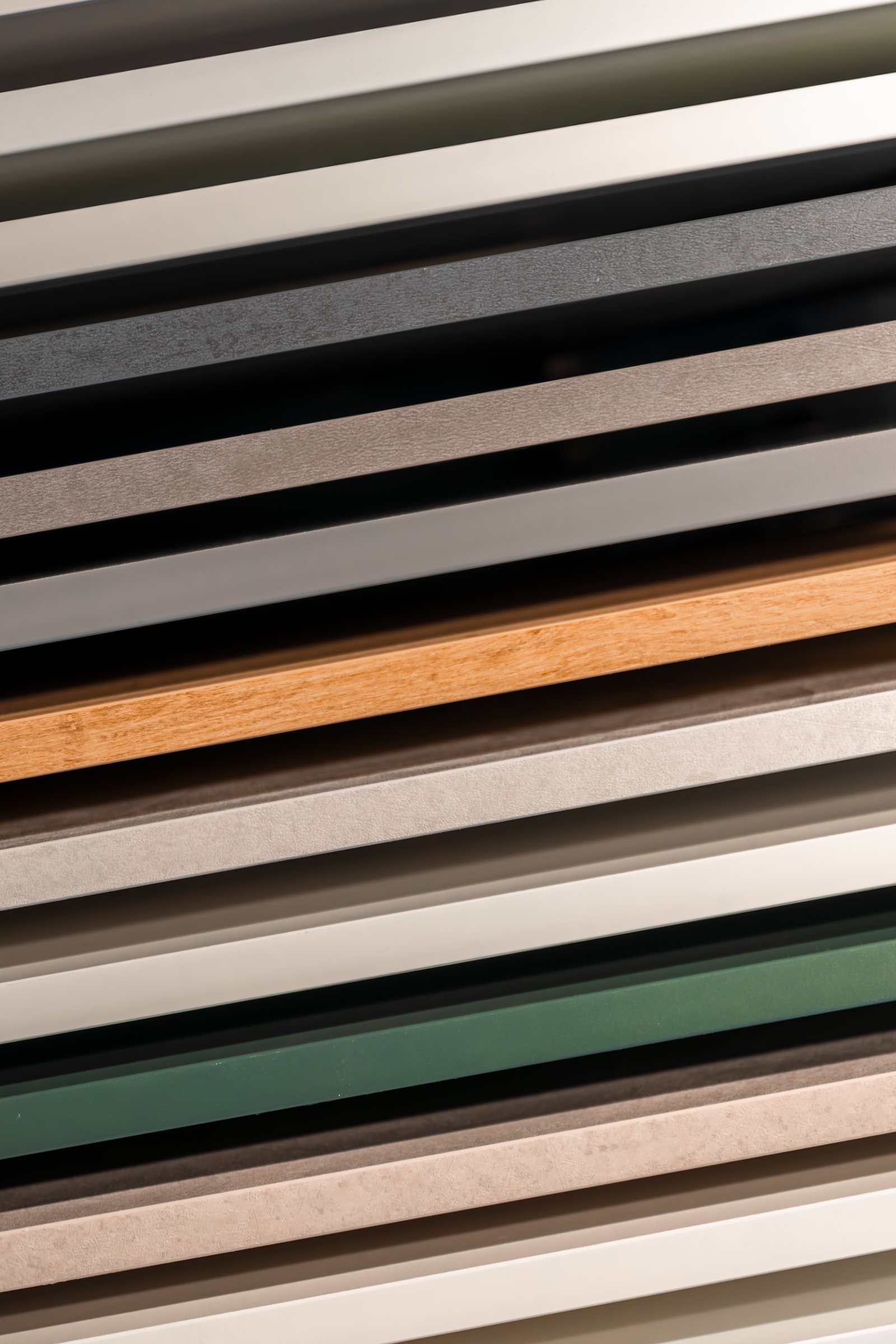 Diagonal stack of cabinet edge-band material samples in varied metal, wood and laminate finishes