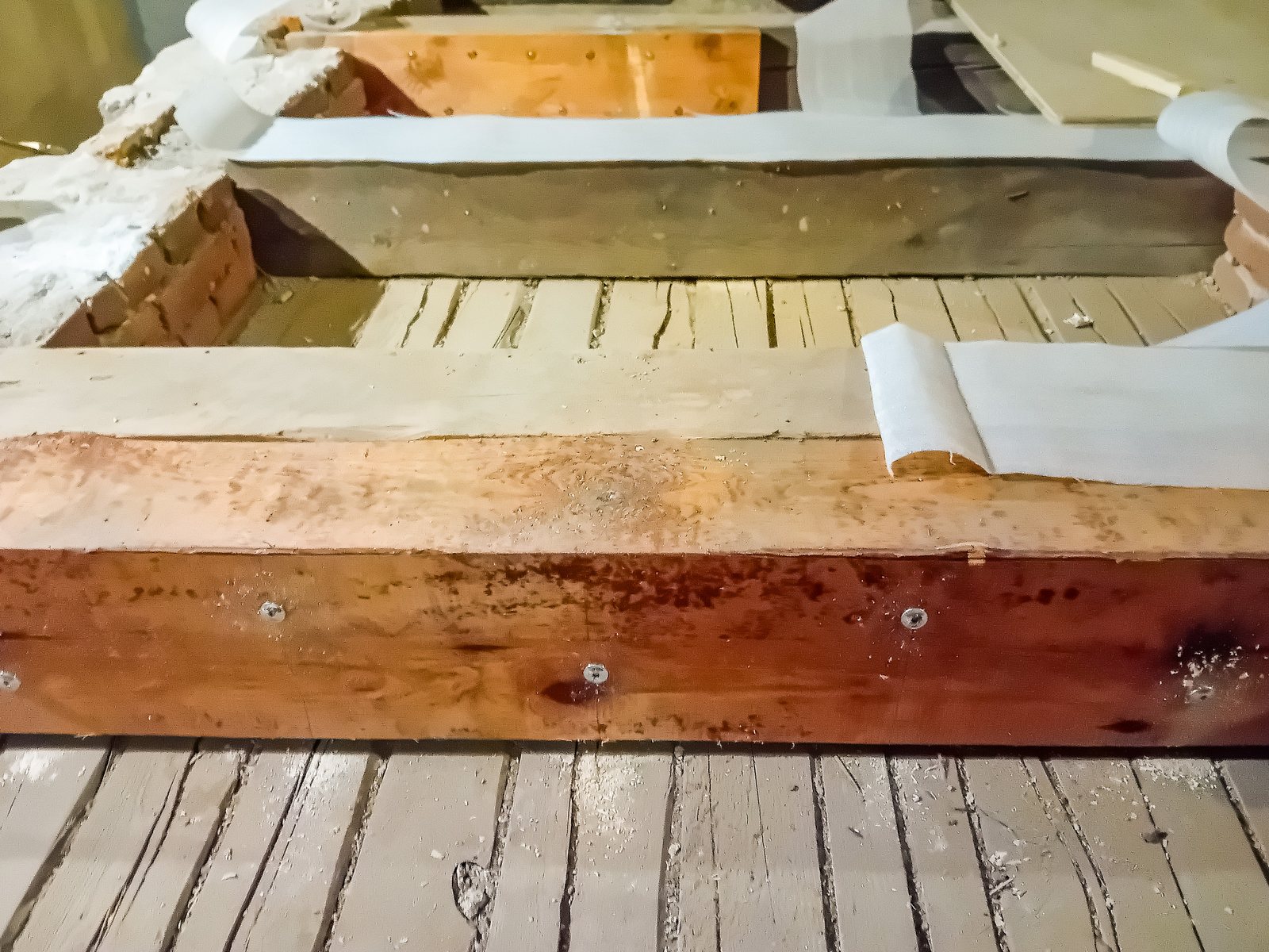 Exposed deck framing during a repair, showing timber joists, waterproof membrane tape and brick side by side