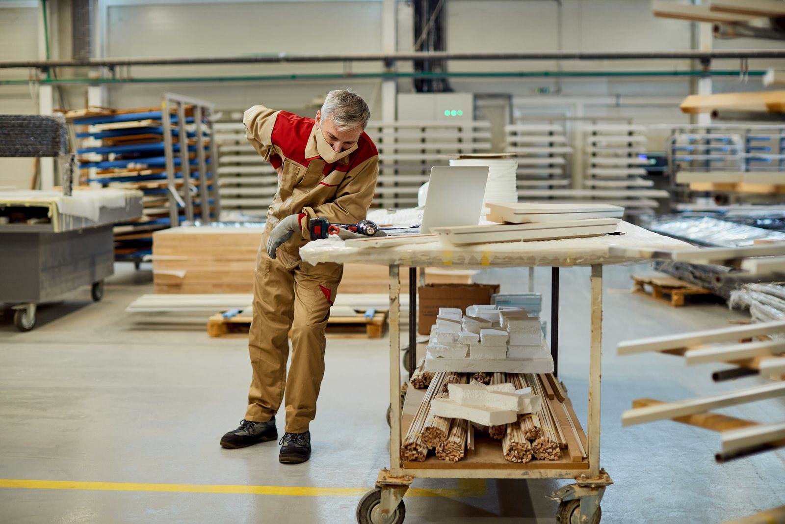 Worker beside a cart of moulding stock and a laptop in a production workshop
