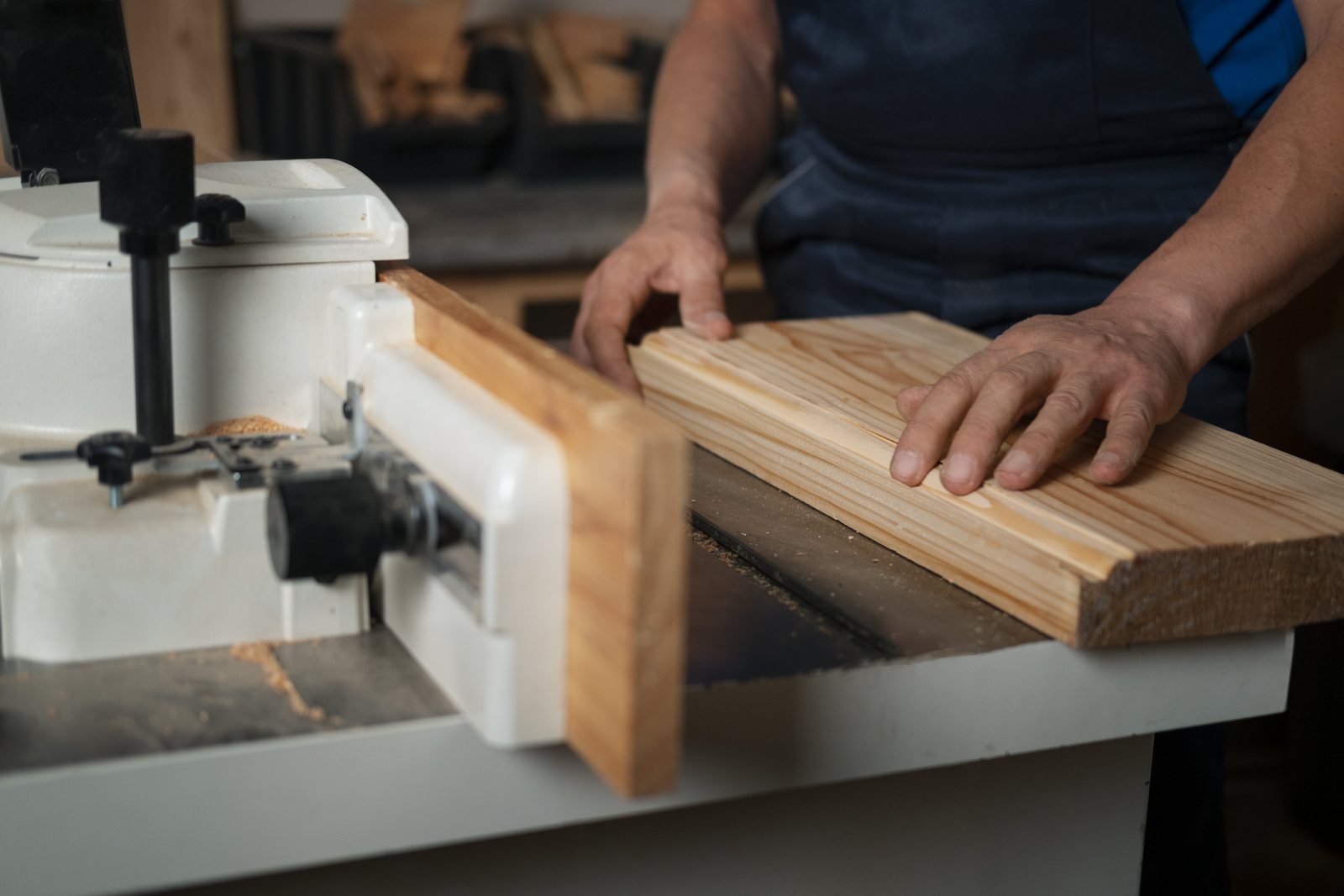 Worker feeding a board through a jointer machine in a wood shop