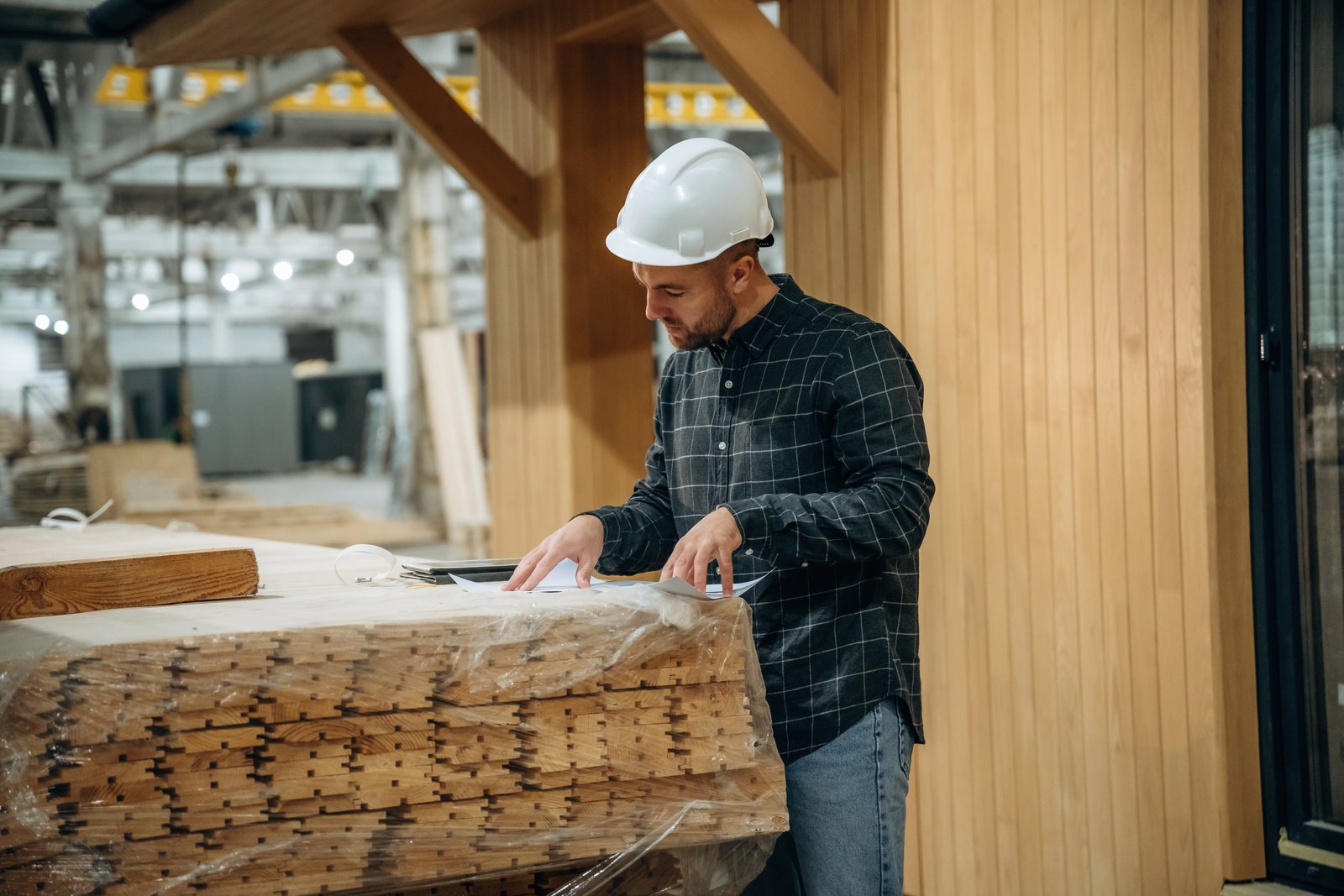 Worker in a hard hat unwrapping bundled millwork panels on a construction site