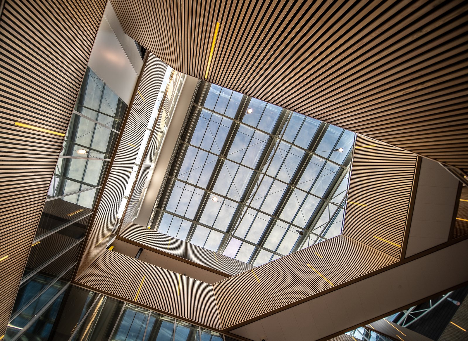 Looking up into a modern atrium with angled wood-slat cladding and a skylight