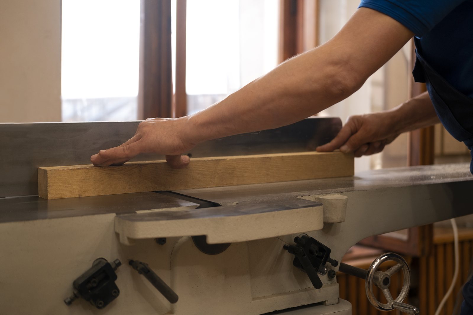 Worker guiding a board through a jointer in a wood shop