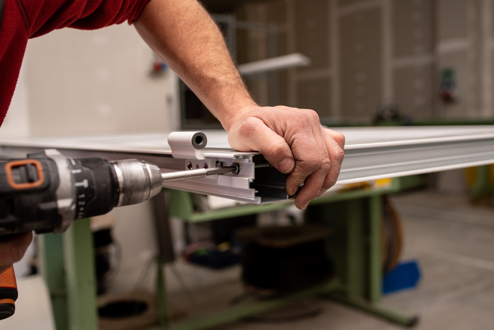 Worker drilling into an aluminium extrusion frame with a power tool