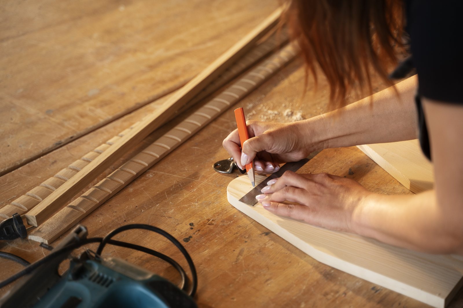 Overhead view of hands marking a wood panel with a pencil and square