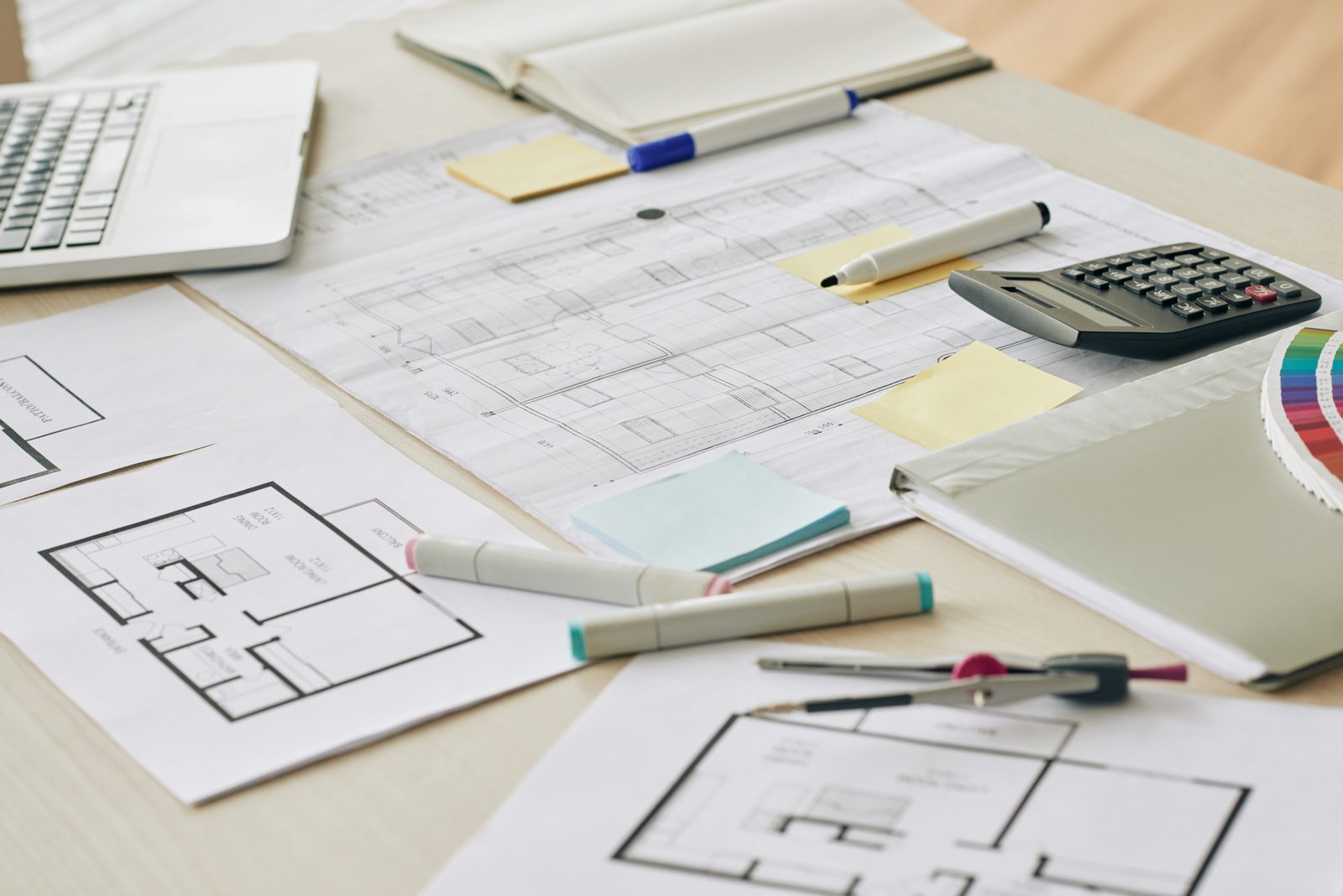 Desk covered with printed floor plans, colour swatches, a calculator and marker pens