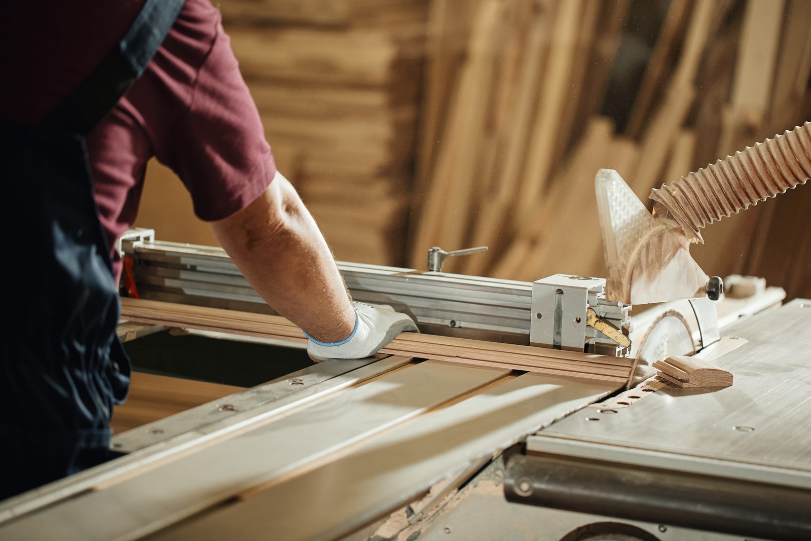 Carpenter guiding a length of timber through a panel saw in a workshop